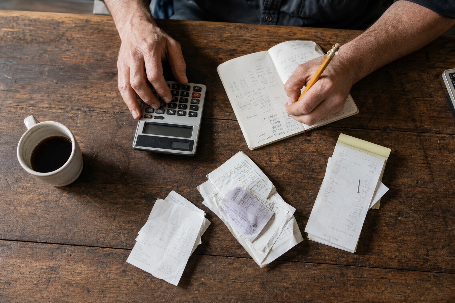 Manos utilizando una calculadora junto a recibos y un cuaderno de gastos