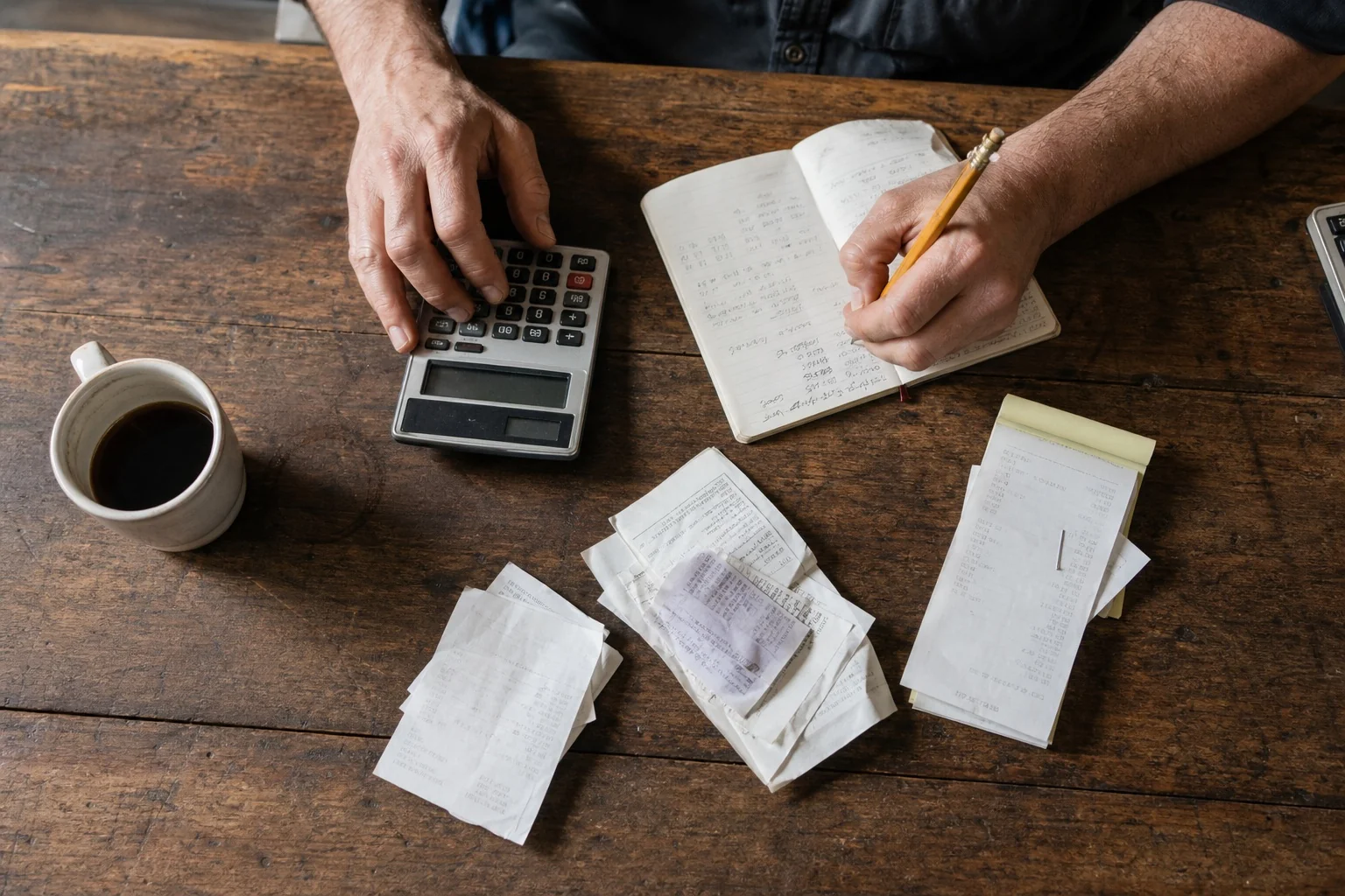 Manos utilizando una calculadora junto a recibos y un cuaderno de gastos